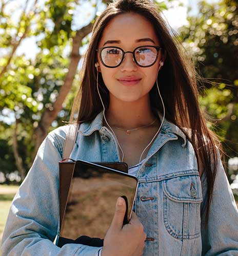 Student outdoors holding a tablet computer and notebook